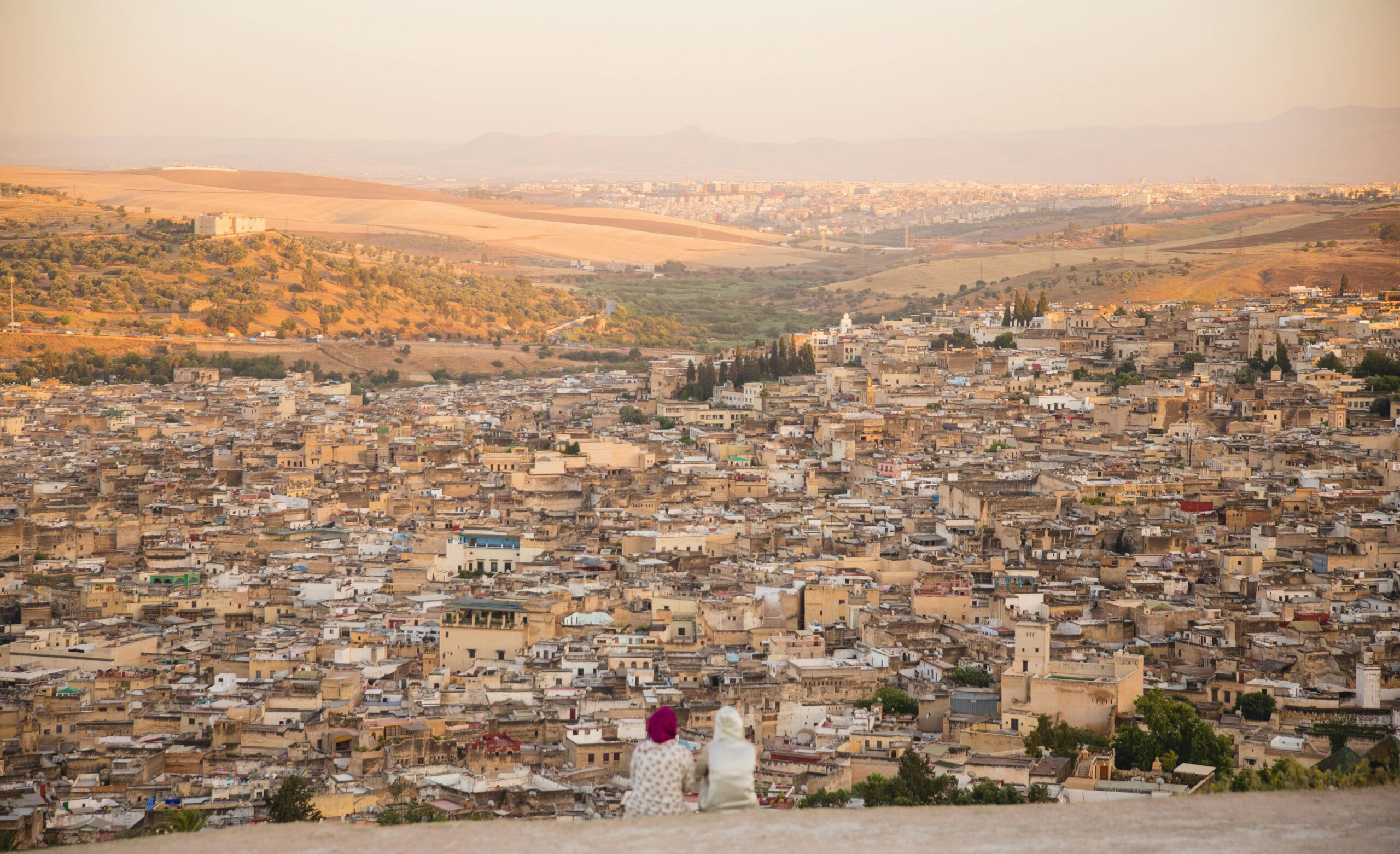 pexels-photo-5472532-5472532 Back view of unrecognizable distant female in traditional wear and headwear sitting on top of mountain above old town with buildings